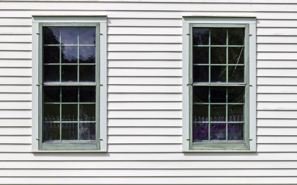 Exterior view of custom double-hung windows with light green frames installed on a white home in Toledo, Ohio.
