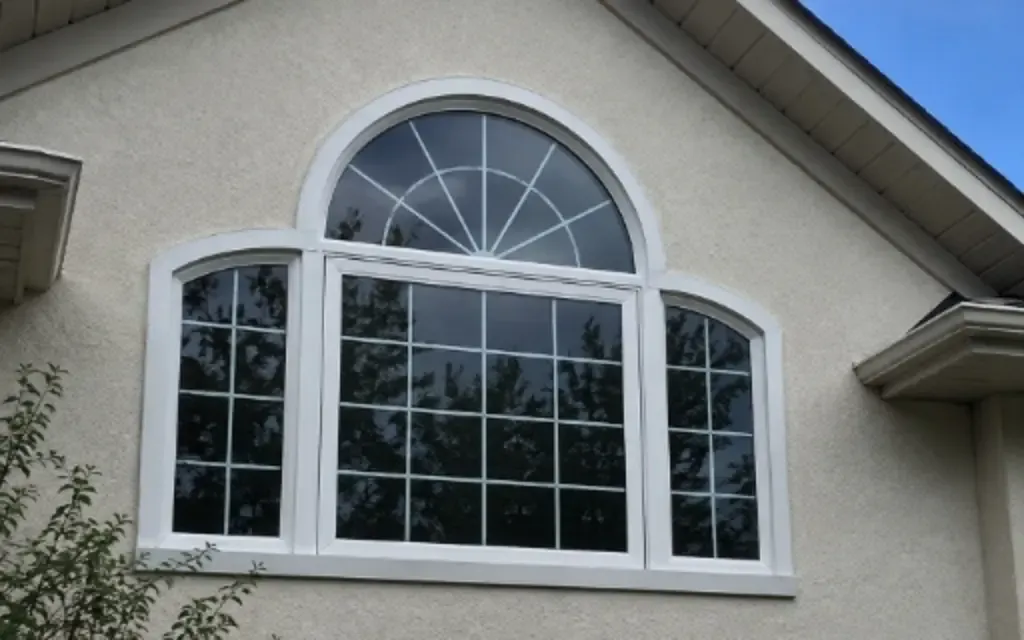 White custom shape window with an arched top and decorative grille installed on a stucco home.