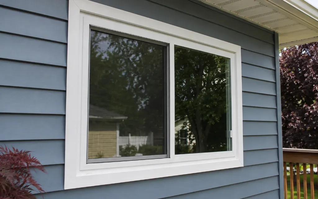 Modern white vinyl sliding replacement window installed on a blue-sided home, providing expansive outdoor views and improved energy efficiency in Findlay, Ohio.