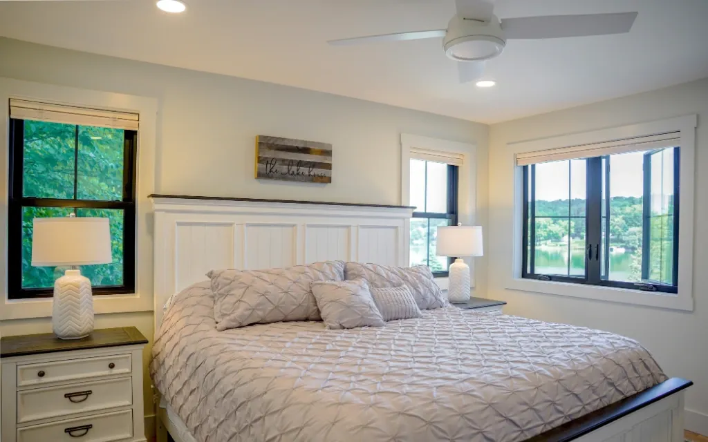 Bedroom with a corner casement window overlooking a lake, black grille pattern, dark window frames.