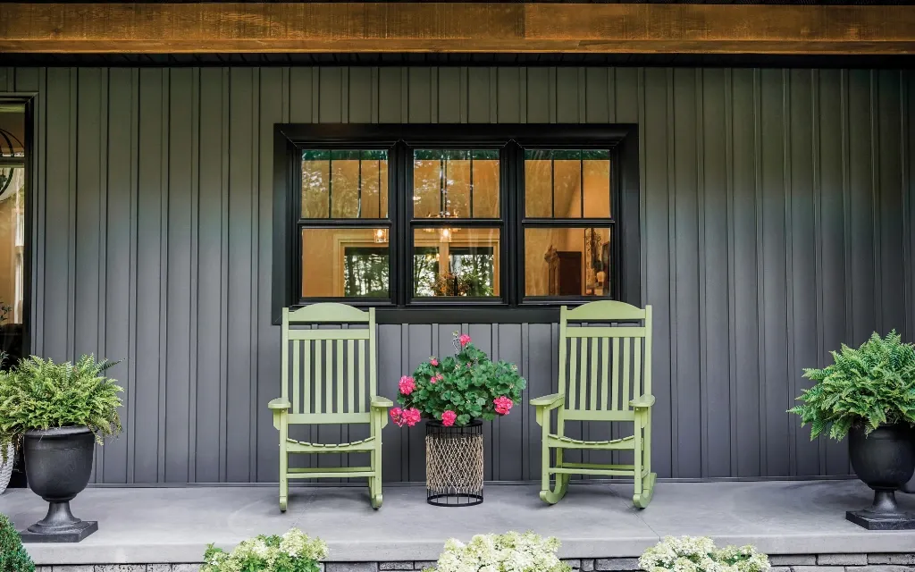 Black double hung windows on a modern dark-sided home with rocking chairs and decorative potted plants on the front porch.