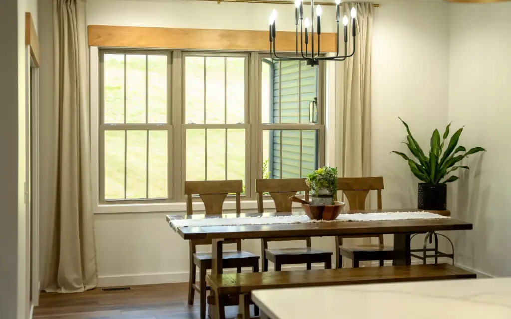 Bright dining room featuring newly installed white double hung replacement windows that fill the space with natural light, complemented by wood trim, neutral curtains, and modern farmhouse décor.