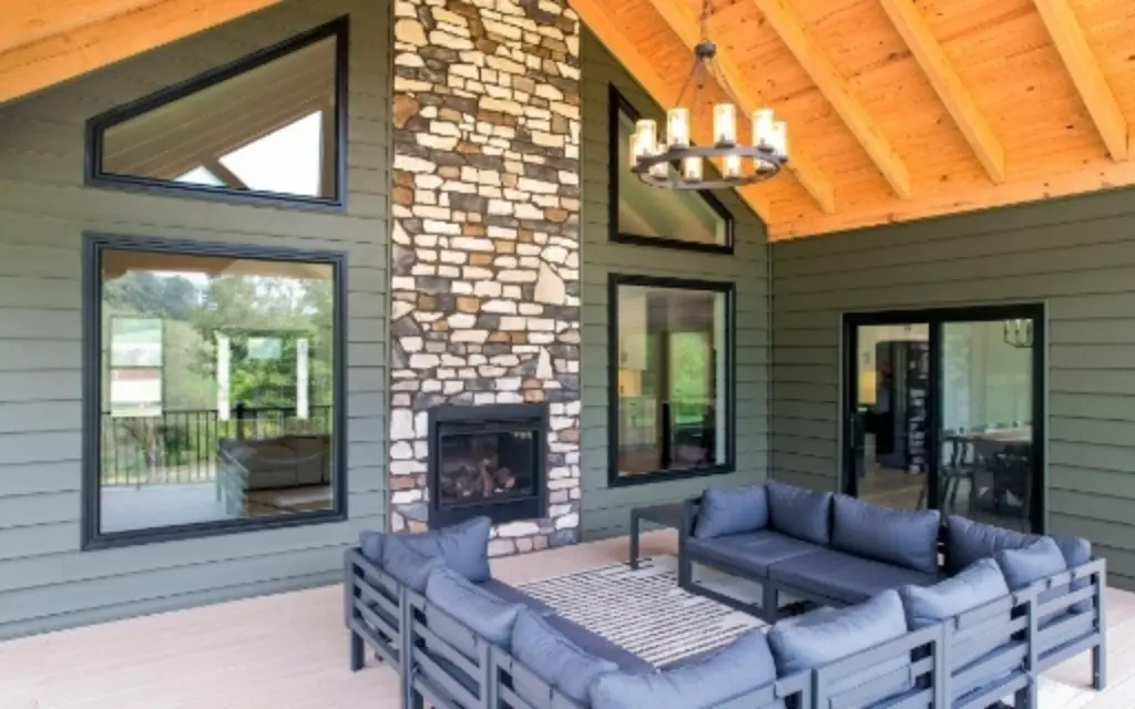Large black-framed picture windows in a covered patio with a stone fireplace and vaulted wood ceiling.